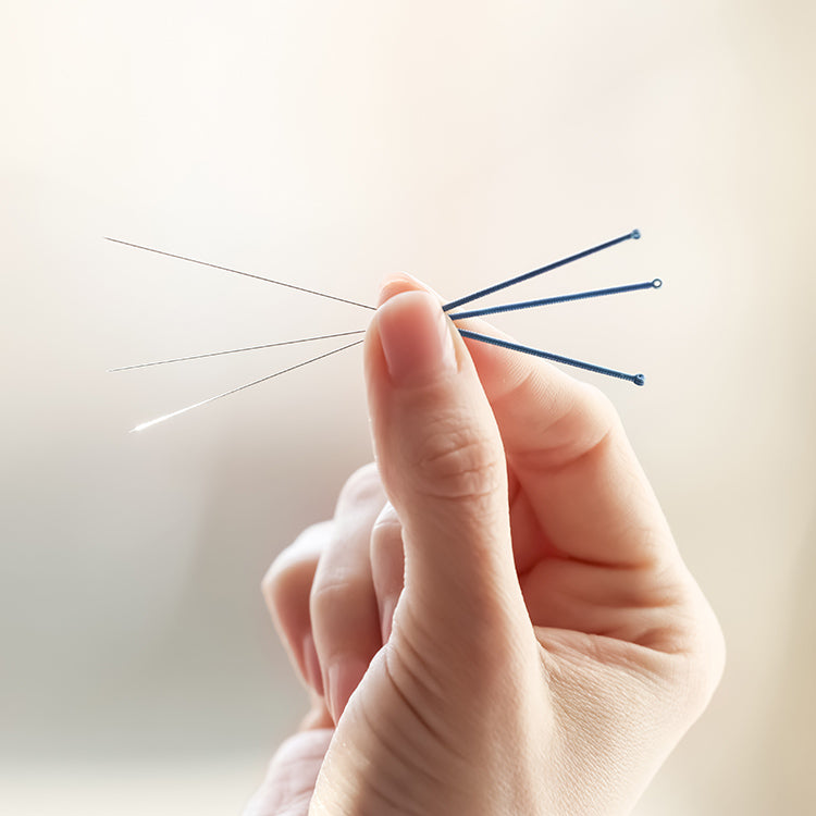 A hand holding acupuncture needles against a light background.