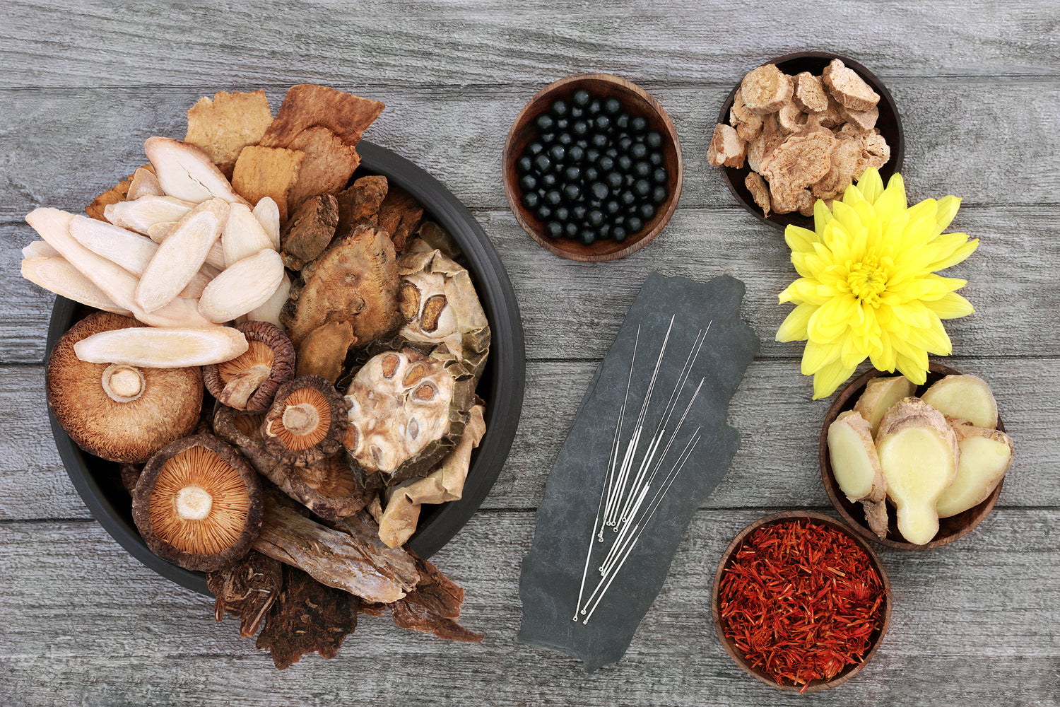 Herbal ingredients including dried herbs and a yellow flower, and acupuncture needles on a wooden surface.