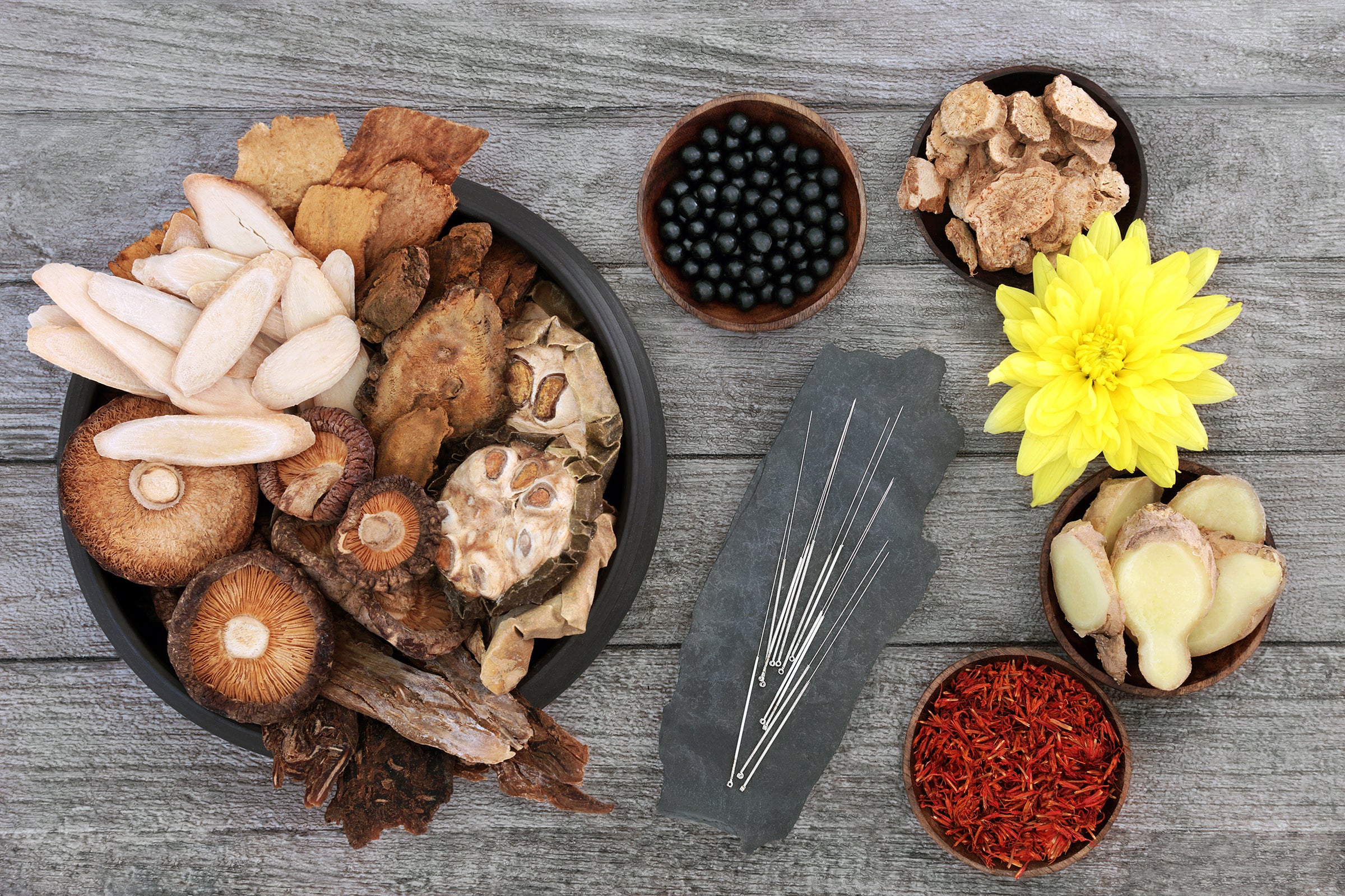Herbal ingredients including dried herbs and a yellow flower, and acupuncture needles on a wooden surface.