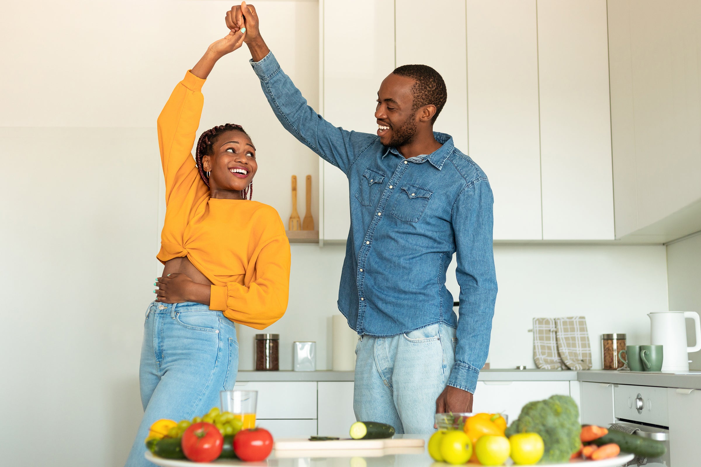 Couple dancing in a kitchen with fruits and vegetables on the counter.