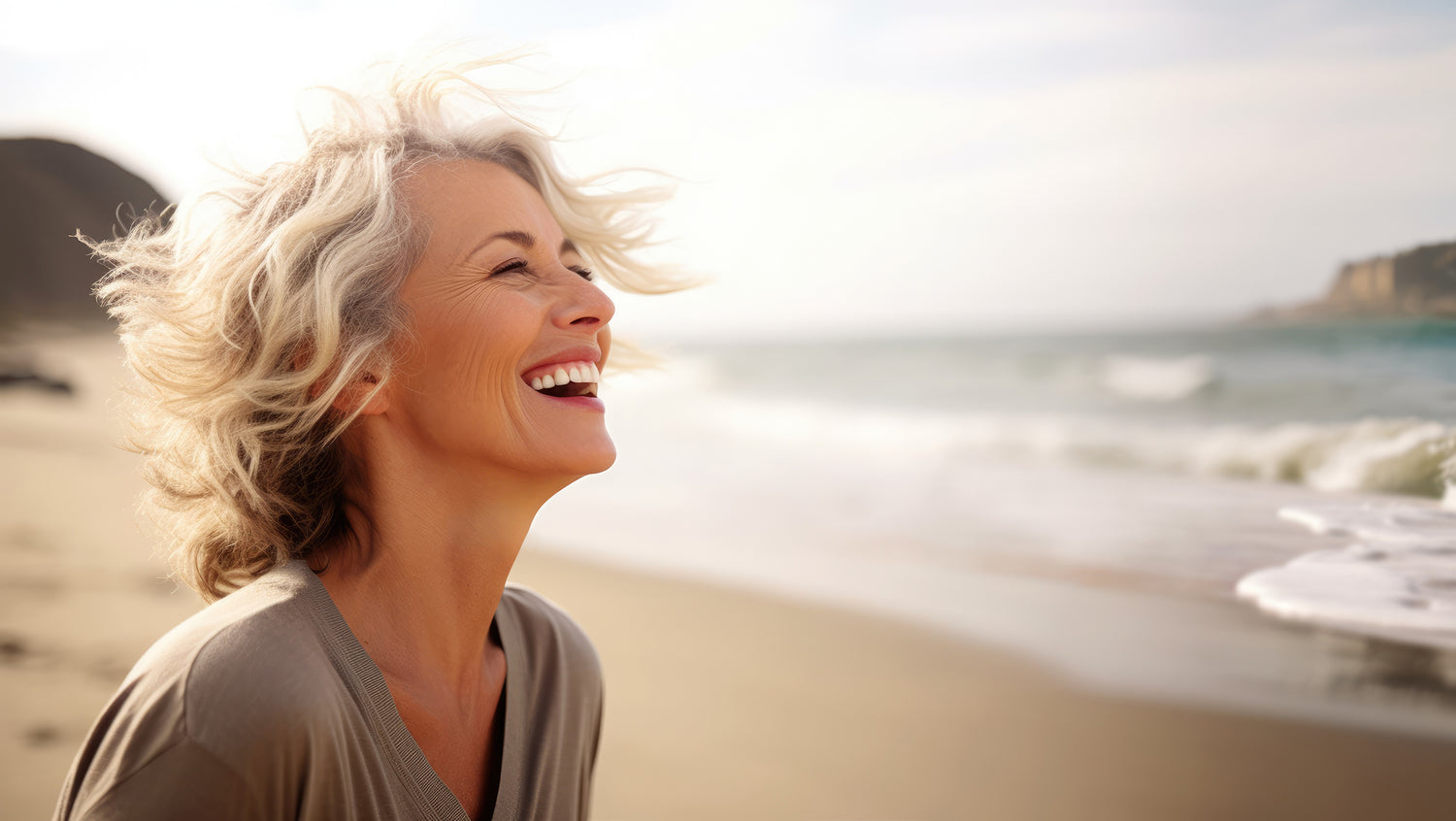 Woman laughing on a beach with ocean waves in the background.