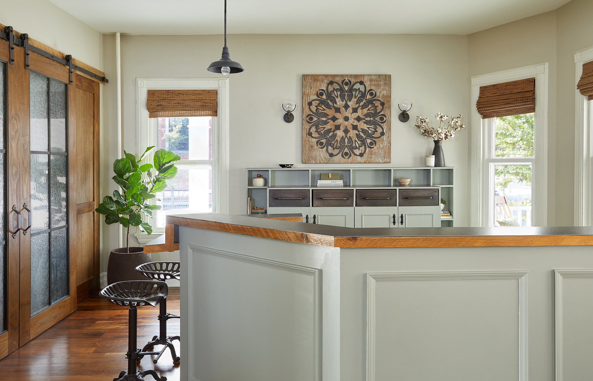 Jennifer Layne reception area with green-gray desk, hardwood floor, stools, windows, and mandala art on the wall
