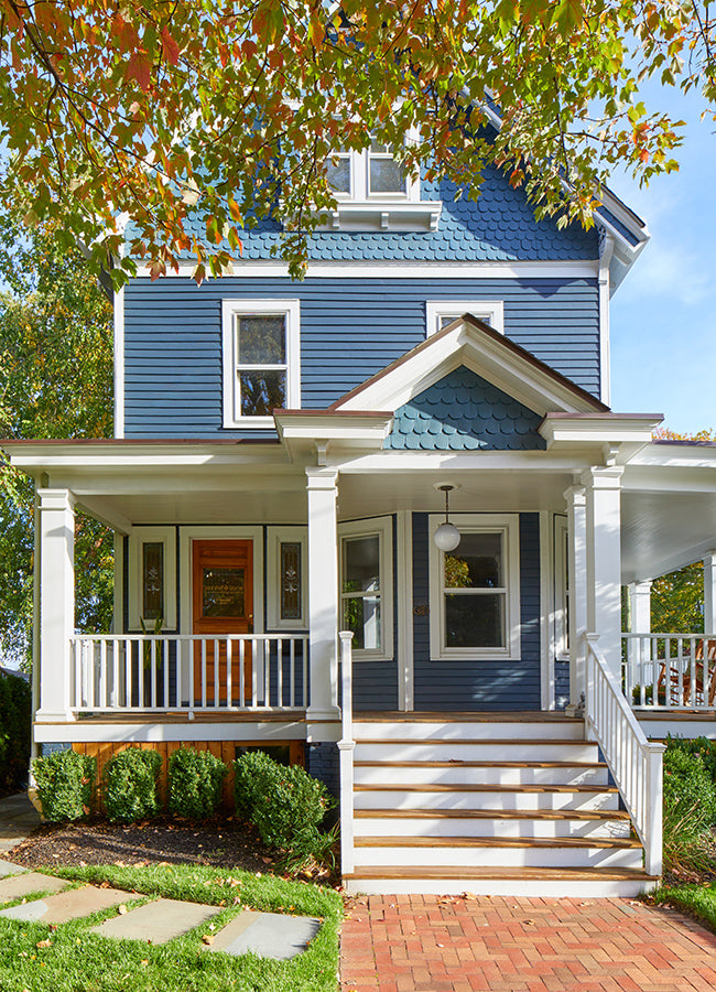 Straight-on view of Jennifer Layne facility, which is a blue house with white porch and steps, surrounded by greenery.