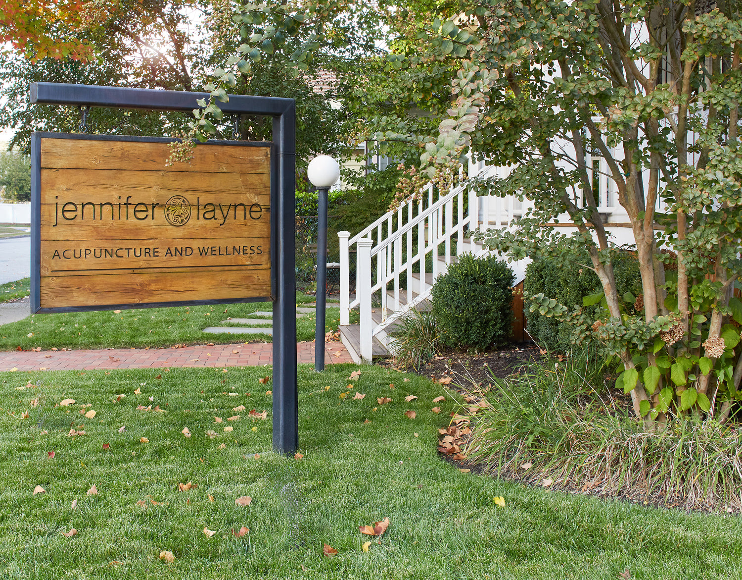 Wooden sign for Jennifer Layne Acupuncture and Wellness in the yard in front of the office