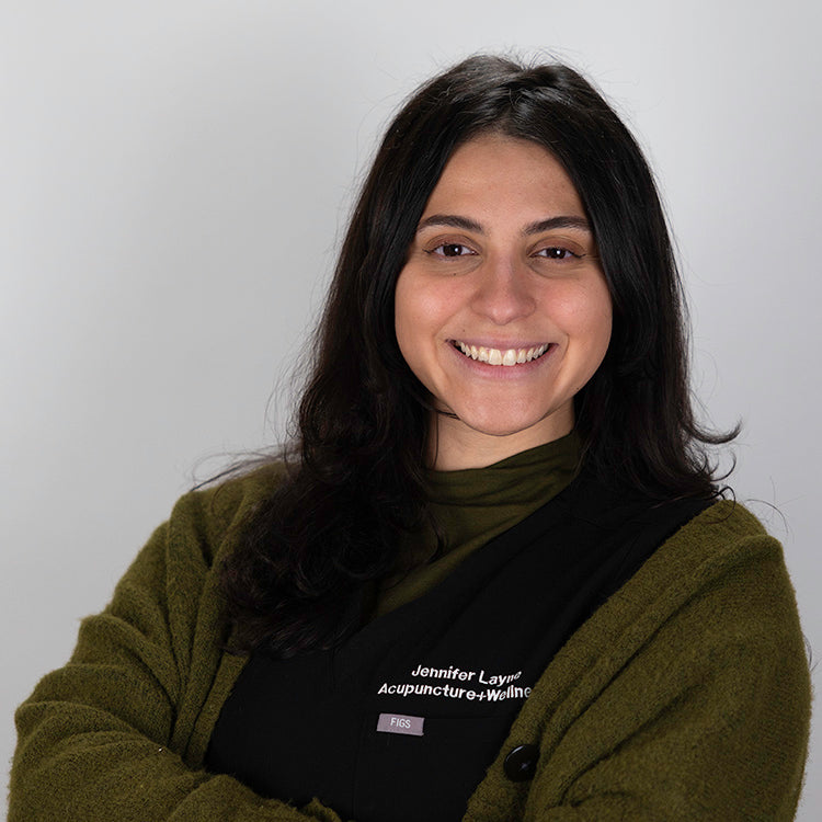 Headshot of Alicia Baez, smiling, wearing black scrubs and a sweater.