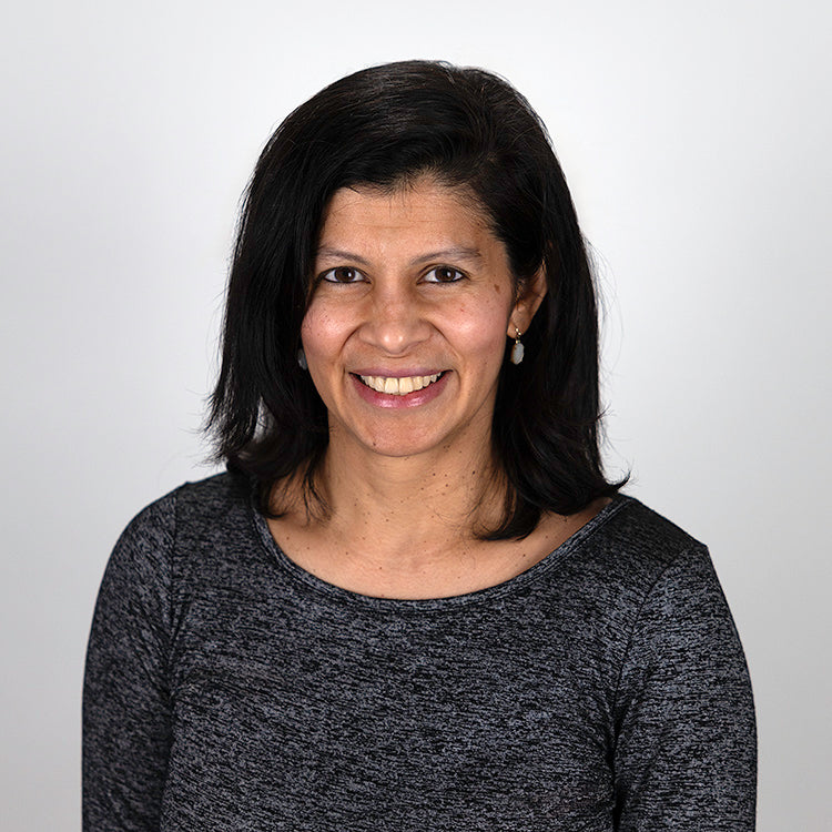 Headshot of Renuka Pinto, smiling, wearing a black and gray shirt.