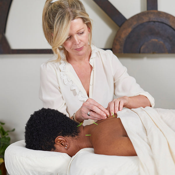 Jennifer Layne McDonald, concentrating, performing acupuncture on a patient's back and neck in a treatment room.