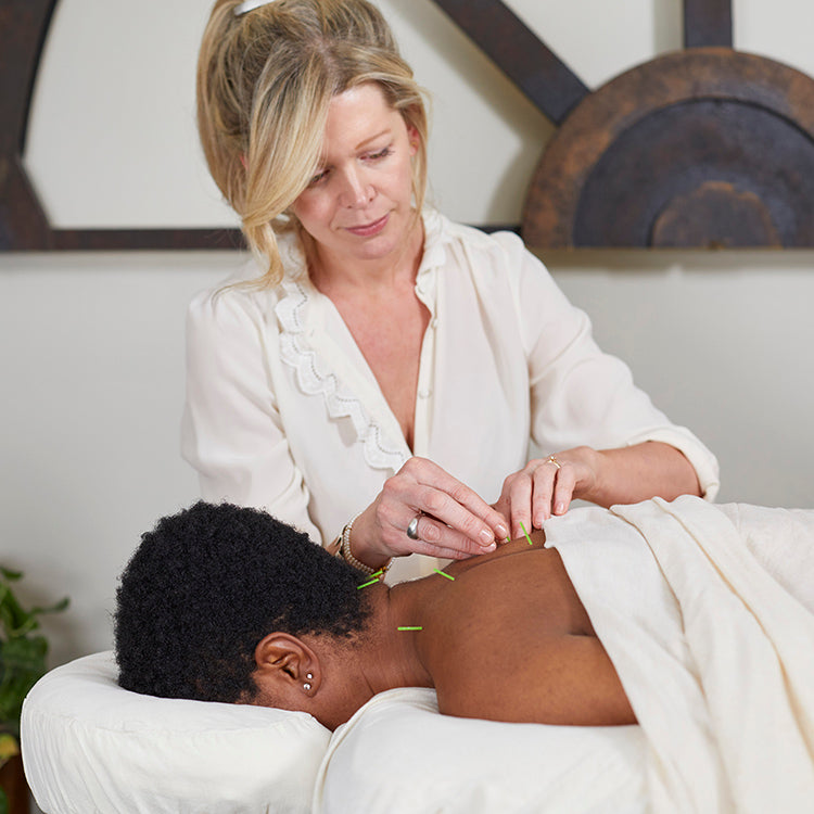 Jennifer Layne McDonald, concentrating, performing acupuncture on a patient's back and neck in a treatment room.