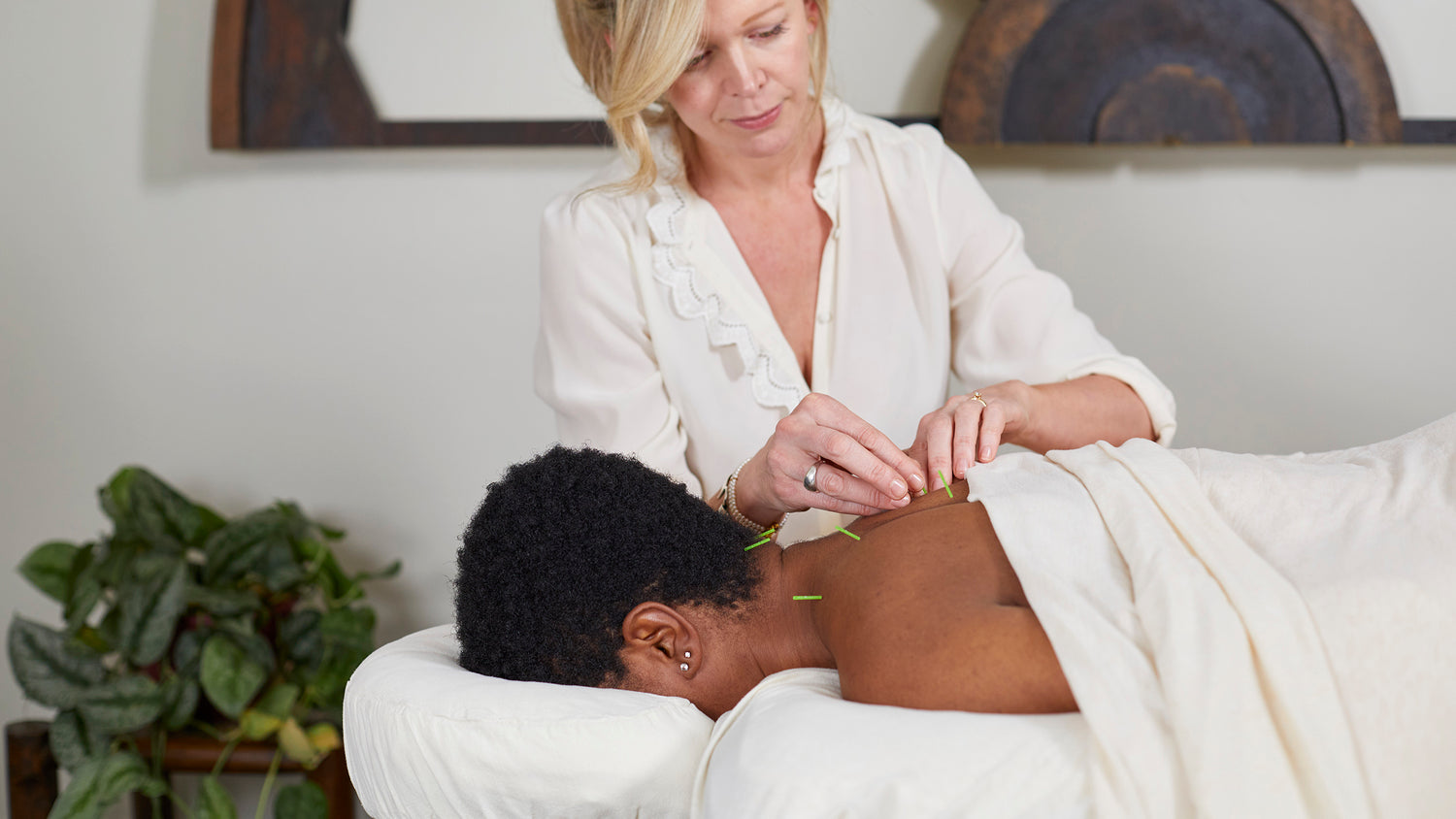 Jennifer Layne McDonald concentrating, performing acupuncture on a patient's back and neck in a treatment room.